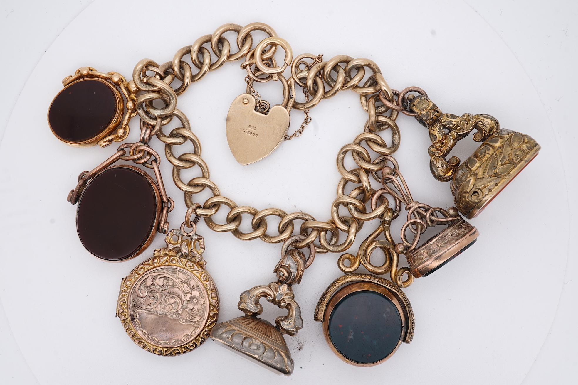 A 1970's 9ct gold curb link charm bracelet, with 9ct gold heart shaped clasp, hung with seven assorted gold or gilt metal mounted charms including six chalcedony set fob seals, gross weight 73 grams.